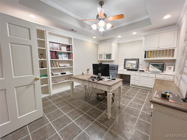 home office with dark tile patterned floors, ornamental molding, ceiling fan, and a tray ceiling