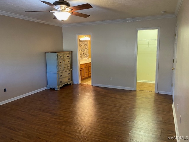 unfurnished bedroom with a closet, dark wood-type flooring, a walk in closet, ornamental molding, and ceiling fan