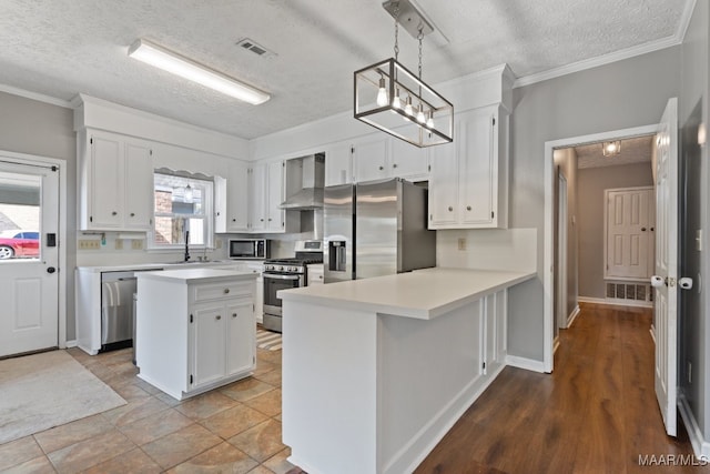 kitchen featuring wall chimney range hood, hanging light fixtures, stainless steel appliances, white cabinets, and a textured ceiling