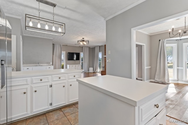 kitchen featuring a kitchen island, hanging light fixtures, ornamental molding, white cabinets, and a textured ceiling