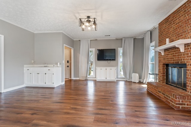 unfurnished living room featuring sink, a textured ceiling, dark hardwood / wood-style flooring, a brick fireplace, and crown molding