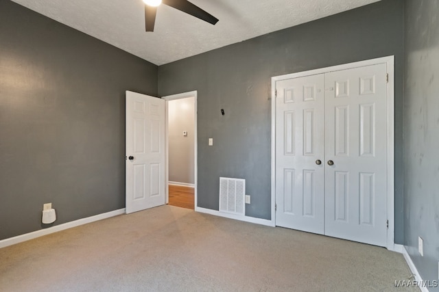 unfurnished bedroom with a closet, a textured ceiling, light colored carpet, and ceiling fan