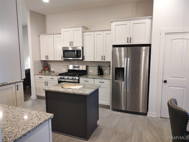 kitchen with decorative backsplash, a kitchen island, light stone counters, white cabinetry, and stainless steel appliances