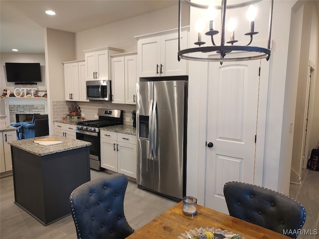 kitchen featuring decorative backsplash, light stone counters, stainless steel appliances, white cabinetry, and a kitchen island