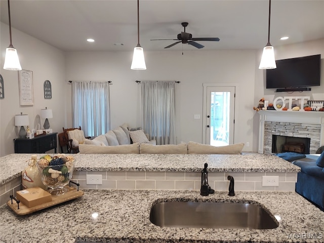 kitchen with light stone countertops, ceiling fan, sink, a fireplace, and hanging light fixtures