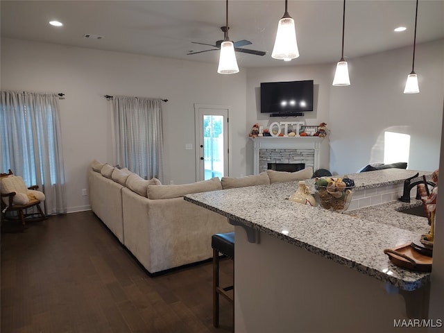 living room featuring a fireplace, ceiling fan, dark wood-type flooring, and sink