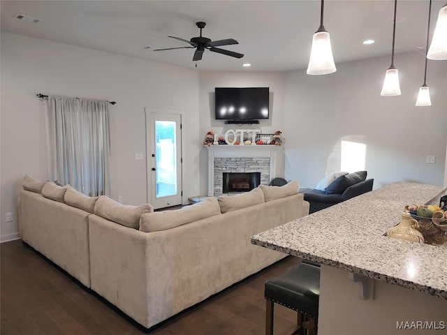 living room with ceiling fan, a stone fireplace, and dark wood-type flooring