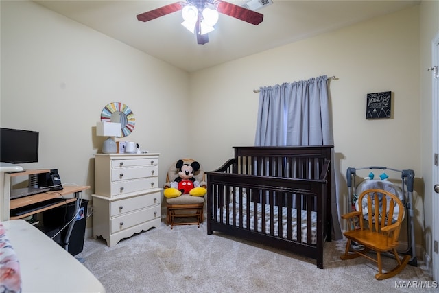 bedroom with a crib, light colored carpet, and ceiling fan