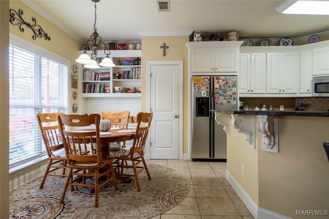 kitchen with appliances with stainless steel finishes, light tile patterned floors, a notable chandelier, white cabinets, and plenty of natural light