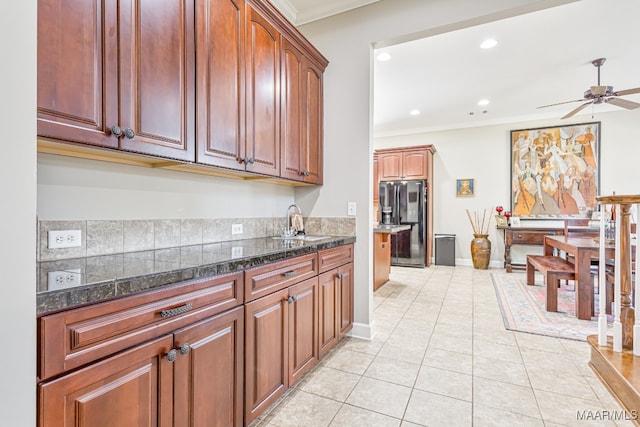 kitchen featuring fridge with ice dispenser, ceiling fan, light tile patterned floors, dark stone counters, and crown molding