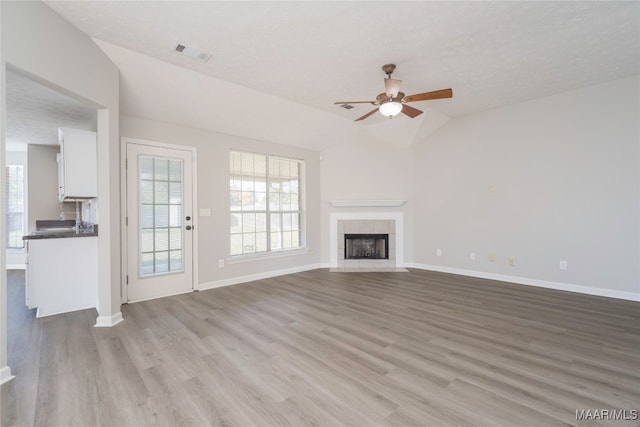 unfurnished living room with ceiling fan, a textured ceiling, lofted ceiling, and light wood-type flooring