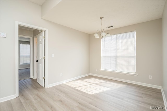 spare room with a wealth of natural light, a chandelier, and light wood-type flooring