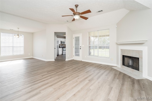 unfurnished living room featuring light hardwood / wood-style floors, lofted ceiling, a textured ceiling, and a tiled fireplace