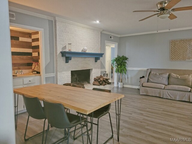 dining room with ornamental molding, hardwood / wood-style flooring, ceiling fan, and a brick fireplace