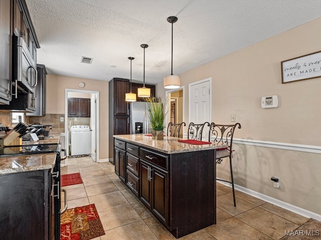 kitchen with light stone countertops, a center island, washer / clothes dryer, pendant lighting, and appliances with stainless steel finishes