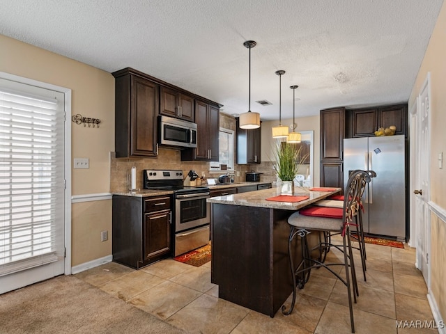 kitchen with pendant lighting, a center island, backsplash, appliances with stainless steel finishes, and a kitchen bar