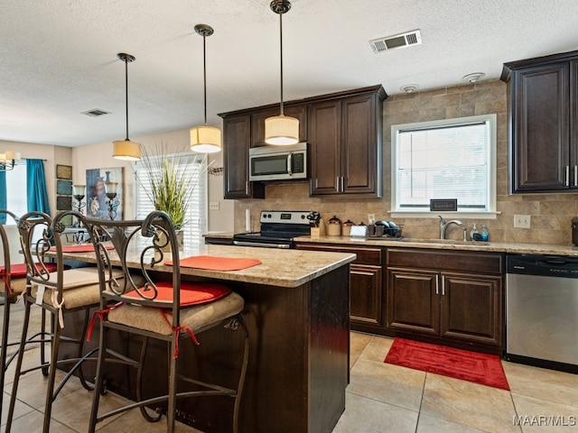 kitchen with a center island, sink, hanging light fixtures, stainless steel appliances, and a breakfast bar