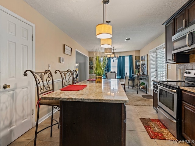 kitchen with a center island, a kitchen breakfast bar, hanging light fixtures, light stone countertops, and appliances with stainless steel finishes