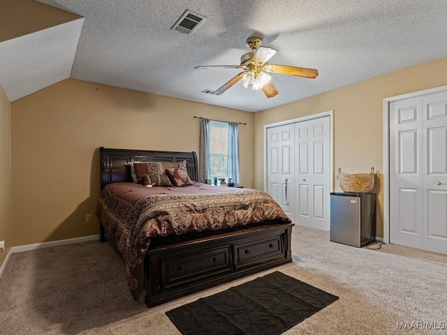 carpeted bedroom featuring stainless steel fridge, a textured ceiling, two closets, vaulted ceiling, and ceiling fan