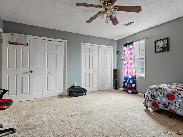 bedroom featuring two closets, a textured ceiling, carpet floors, and ceiling fan