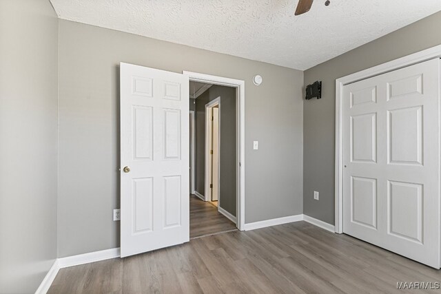 unfurnished bedroom featuring a closet, light hardwood / wood-style floors, a textured ceiling, and ceiling fan