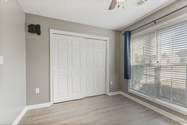 unfurnished bedroom featuring a closet, ceiling fan, a textured ceiling, and light hardwood / wood-style flooring