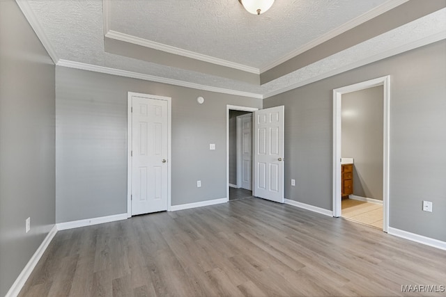 unfurnished bedroom featuring ornamental molding, light hardwood / wood-style flooring, a textured ceiling, and ensuite bath