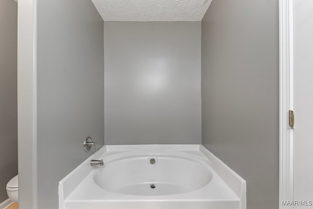 bathroom with toilet, a textured ceiling, and a tub to relax in