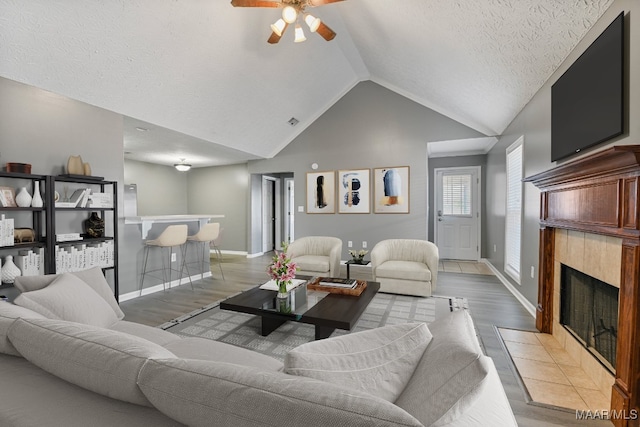 living room with ceiling fan, a textured ceiling, high vaulted ceiling, a fireplace, and light hardwood / wood-style floors