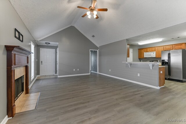 unfurnished living room featuring a tile fireplace, vaulted ceiling, a textured ceiling, light hardwood / wood-style floors, and ceiling fan