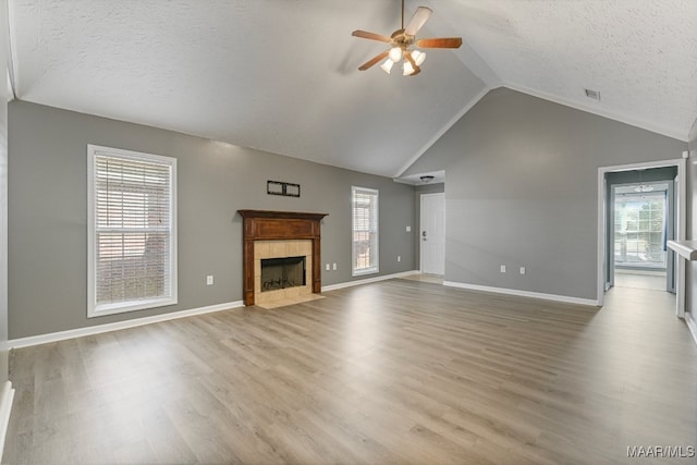 unfurnished living room featuring a tile fireplace, a textured ceiling, light wood-type flooring, and ceiling fan