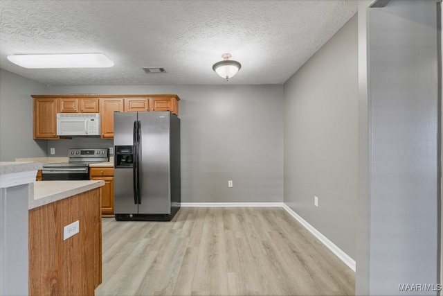 kitchen featuring appliances with stainless steel finishes, a textured ceiling, and light hardwood / wood-style floors