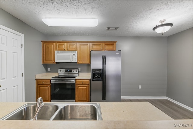 kitchen with stainless steel appliances, a textured ceiling, sink, and hardwood / wood-style floors