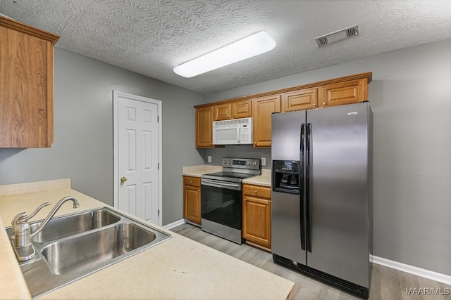 kitchen featuring sink, stainless steel appliances, a textured ceiling, and light hardwood / wood-style flooring