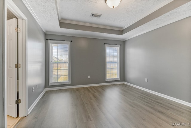 spare room with ornamental molding, a healthy amount of sunlight, a tray ceiling, and light wood-type flooring