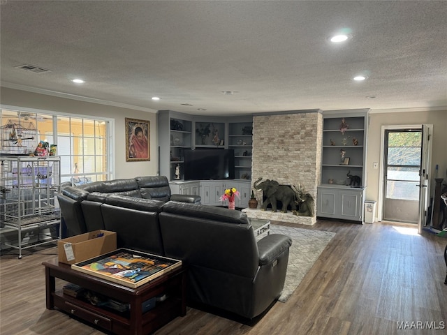 living room with a stone fireplace, wood-type flooring, ornamental molding, a textured ceiling, and built in shelves