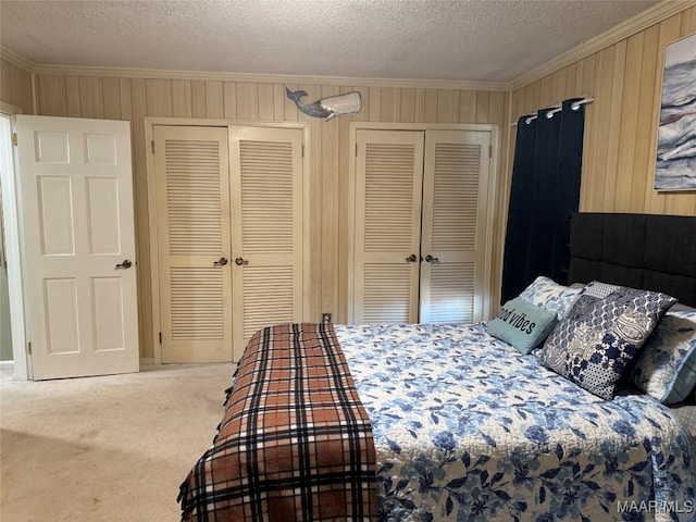 bedroom featuring light carpet, crown molding, a textured ceiling, and two closets