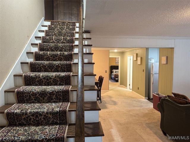 stairs with carpet, a textured ceiling, and ornamental molding