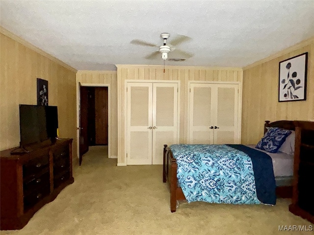 carpeted bedroom featuring ornamental molding, two closets, a textured ceiling, and ceiling fan