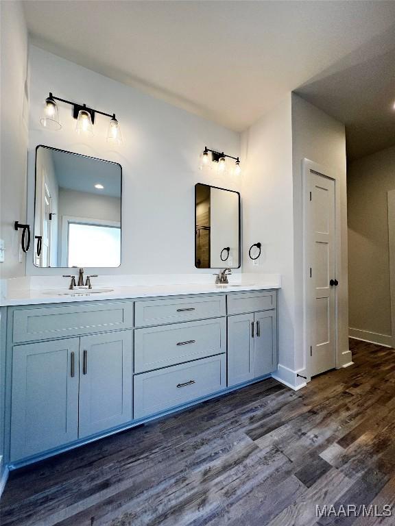 full bath with double vanity, a sink, baseboards, and wood finished floors