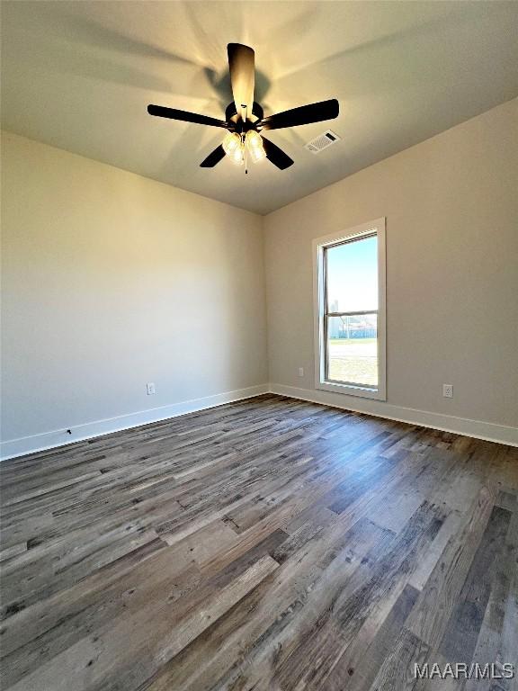 spare room featuring a ceiling fan, dark wood finished floors, visible vents, and baseboards