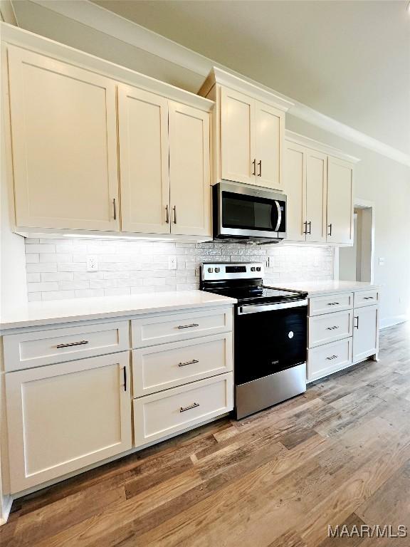 kitchen featuring light countertops, backsplash, appliances with stainless steel finishes, white cabinetry, and wood finished floors