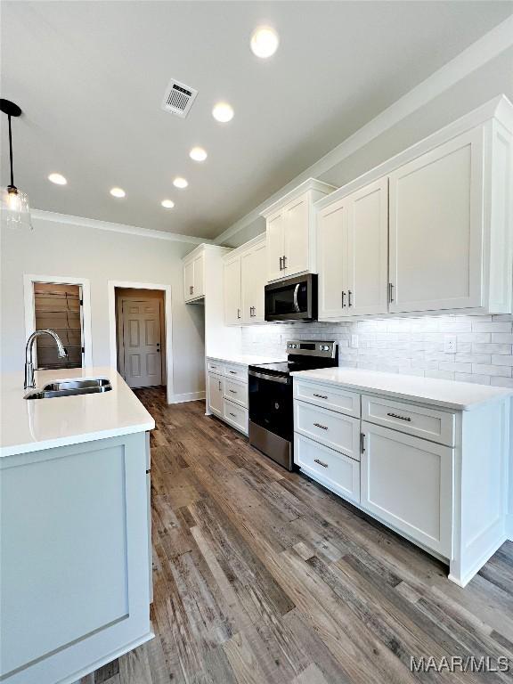 kitchen with white cabinets, appliances with stainless steel finishes, light countertops, pendant lighting, and a sink