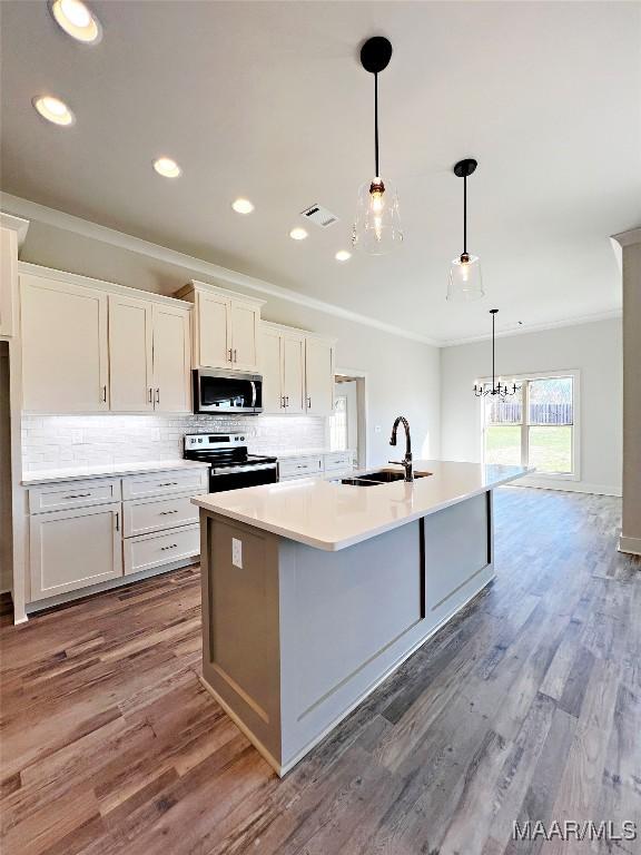 kitchen with stainless steel appliances, a sink, white cabinets, light countertops, and a center island with sink