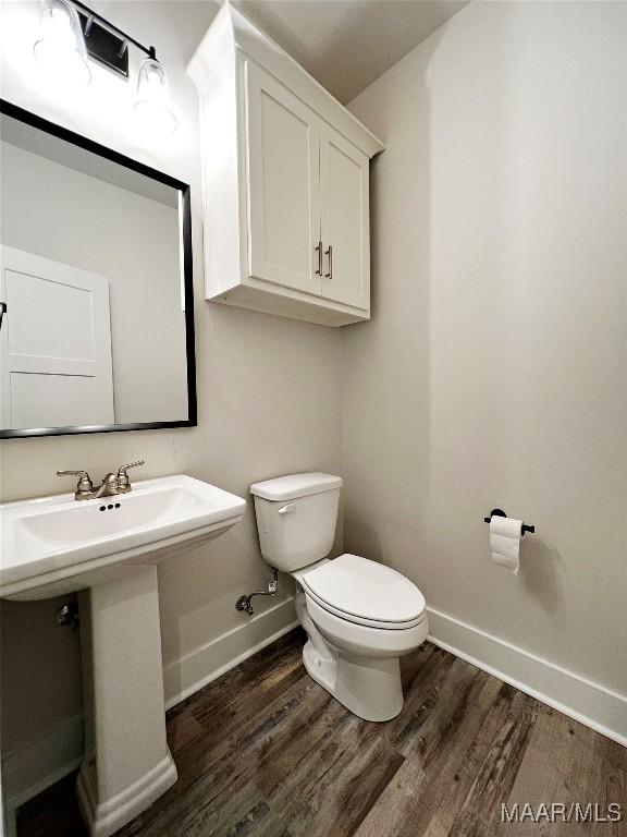 half bath featuring baseboards, toilet, and wood finished floors