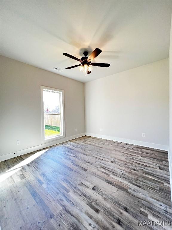 unfurnished room featuring a ceiling fan, wood finished floors, visible vents, and baseboards