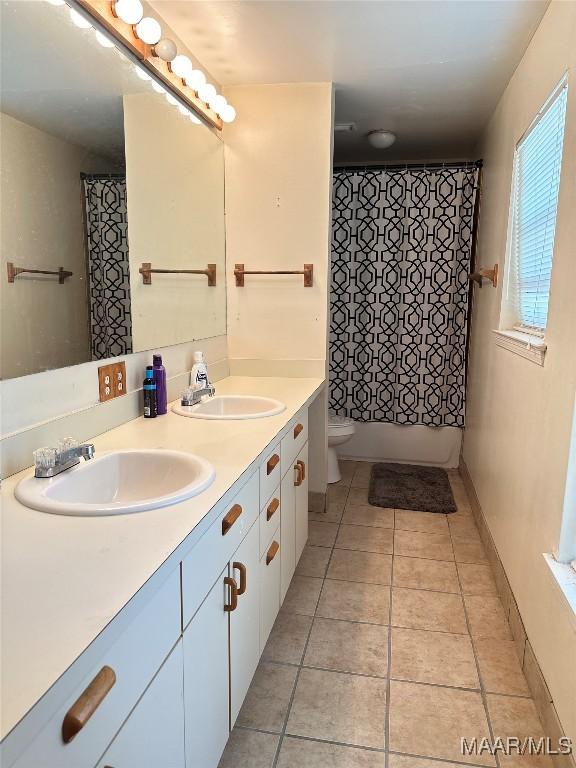 full bath featuring double vanity, a sink, toilet, and tile patterned floors