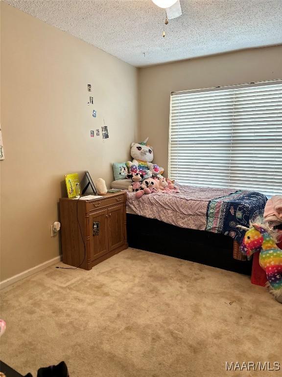 bedroom featuring light carpet, a textured ceiling, a ceiling fan, and baseboards