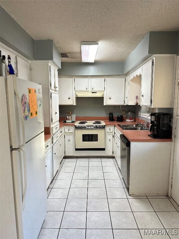 kitchen with white appliances, light tile patterned floors, under cabinet range hood, white cabinetry, and a sink