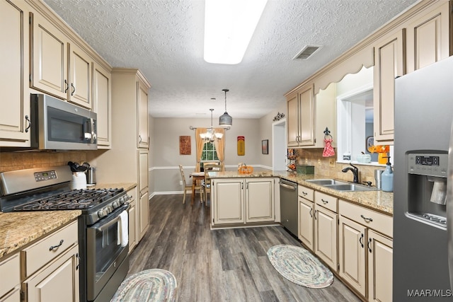 kitchen featuring kitchen peninsula, sink, decorative light fixtures, appliances with stainless steel finishes, and dark hardwood / wood-style flooring